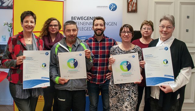 Christopher Winter vom LSB (Mitte) und Verena Mundorf vom Kreissportbund Rheinisch-Bergischer Kreis (2.v.l.) freuen sich mit Anne Paweldyk (1.v.l.), Bernhard Pautsch (3.v.l.), Sabine Kosse (3.v.r.), einer Teilnehmerin des Bewegungsangebots (2.v.r.) und Gertrude Struminski vom RBS (1.v.r.).