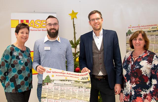 Anne Paweldyk, Dominik Vogt (v.l.) und Irina Herz (1.v.r.) vom ASB Bergisch Land präsentieren mit Manuel Bast von der Bürgerstiftung Leverkusen das Programm des Lebendigen Adventskalenders.