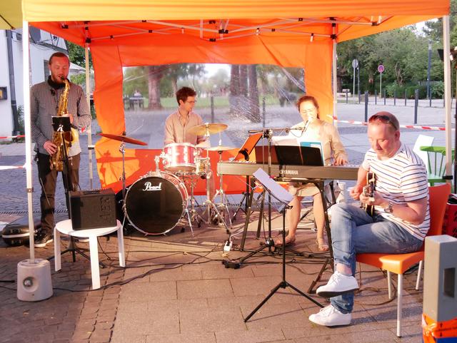 Junodori im orangenen Pavillon vor Mines Spatzentreff: Judith Nordbrock, Gesang und Piano, mit Sergii Chernenko, Saxophon und Querflöte, und Carl Zinsius, Schlagzeug. Als Gastmusiker Torben Jahnke, Gitarre.
